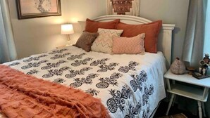 A bedroom with a bed, pillows, a nightstand, a lamp, a wall hanging, and a small table with a figurine. - Boho Bungalow off Main-one block from Lovely Park (Richmond)