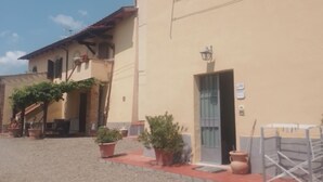 A building with a beige facade, a red roof, and a small garden area with potted plants. - Torre Prima 1 (San Gimignano)