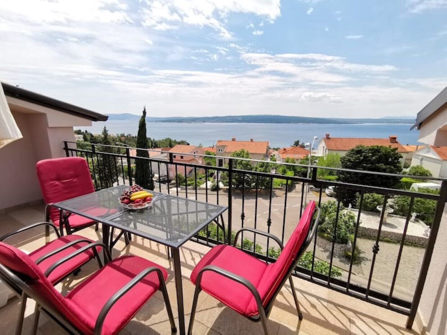 A balcony with a table and chairs, a view of a body of water, and surrounding buildings.