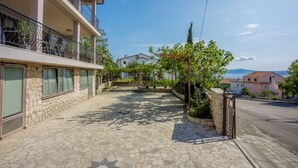 Un cortile lastricato in pietra con cielo sereno, un balcone con ringhiere in metallo e vista sul mare in lontananza.