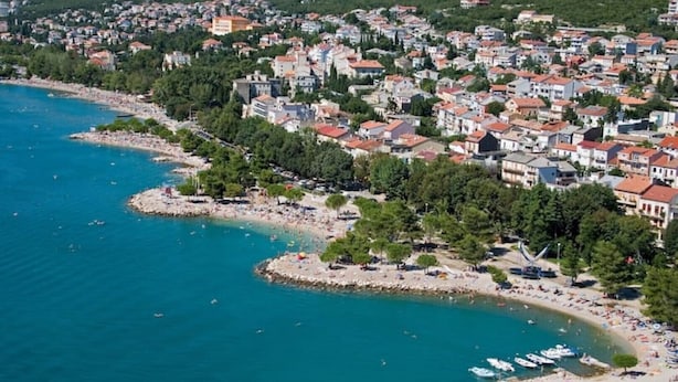 Vista aerea di una cittadina costiera con spiaggia, imbarcazioni e edifici residenziali.