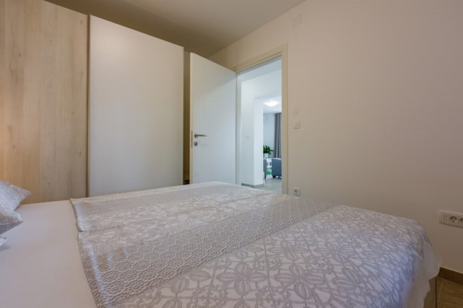 A bedroom with a bed, a wooden wardrobe, and a door leading to another room.
