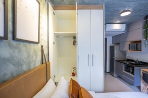 Un dormitorio con cama, armario y kitchenette equipada con refrigerador y microondas.