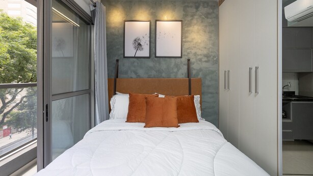 Un dormitorio con una cama grande, una ventana con cortinas, cabecero y vistas al exterior.