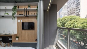 Una habitación de hotel moderna con cama, escritorio y silla, televisor montado en la pared y balcón con vista a la ciudad.