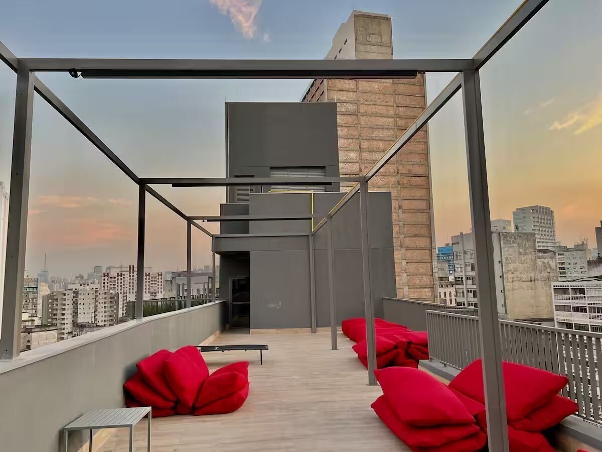 Terraço no telhado com vista para o horizonte urbano, um edifício moderno e almofadas vermelhas.