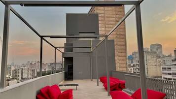 Terraço no telhado com vista para o horizonte urbano, um edifício moderno e almofadas vermelhas.