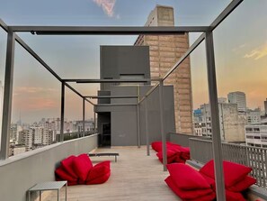 Una terraza en la azotea con vistas al horizonte de la ciudad, un edificio moderno y cojines rojos.