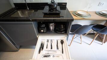 Uma cozinha com bancada preta, pia, fogão e gaveta com utensílios.