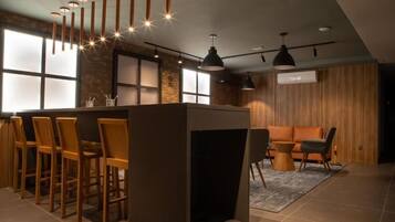 Uma área de bar moderna com cadeiras de madeira, balcão, iluminação pendente e um espaço de estar com sofá e poltronas.