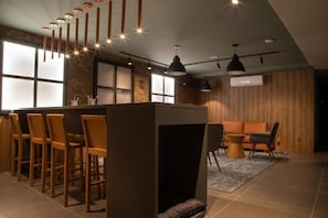 A modern bar area with wooden chairs, a bar counter, pendant lighting, and a seating area with a sofa and chairs.