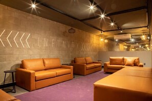 A modern lounge area with sofas arranged in a U-shape, a wall with a geometric light installation, and pendant lighting.