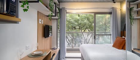 A modern room with a bed, a desk with plates, a TV, and a balcony with curtains.
