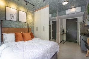 A modern bedroom with a large bed, white bedding, and a headboard. There is a wardrobe with sliding doors and a small bedside table with a lamp. - VN Consolação (São Paulo)