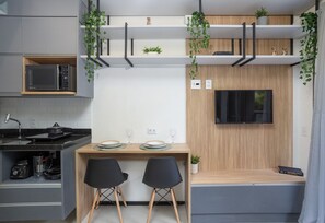 Cocina compacta equipada con microondas, estufa y lavaplatos. Comedor con dos sillas y una mesa. Un televisor está montado en la pared.