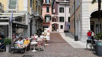 Una strada acciottolata con tavolini all'aperto in un caffè, circondata da edifici storici con balconi e persiane.