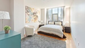 Ein modernes Schlafzimmer mit einem großen Bett, einem Schreibtisch, einem Stuhl und Blick auf die Stadt durch das Fenster.