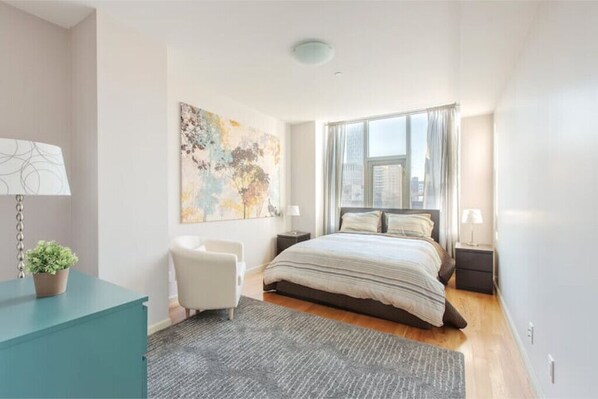 Un dormitorio moderno con una cama grande, un escritorio, una silla y vistas a la ciudad a través de la ventana.