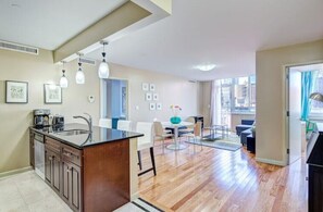Una cocina moderna con una isla central, comedor con mesa y sillas, y vistas de la ciudad a través de amplios ventanales.