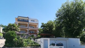 Un immeuble à plusieurs étages doté de balcons, d’un mur en pierre et d’une voiture blanche garée dans un garage.