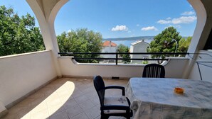 Un balcon avec une table et des chaises, une vue sur la mer et les bâtiments, et un sol carrelé.