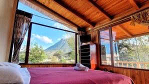 A bedroom with a bed, large windows, and a view of a mountain. - Refugio Cumanda  Lodge (San Pablo del Lago)