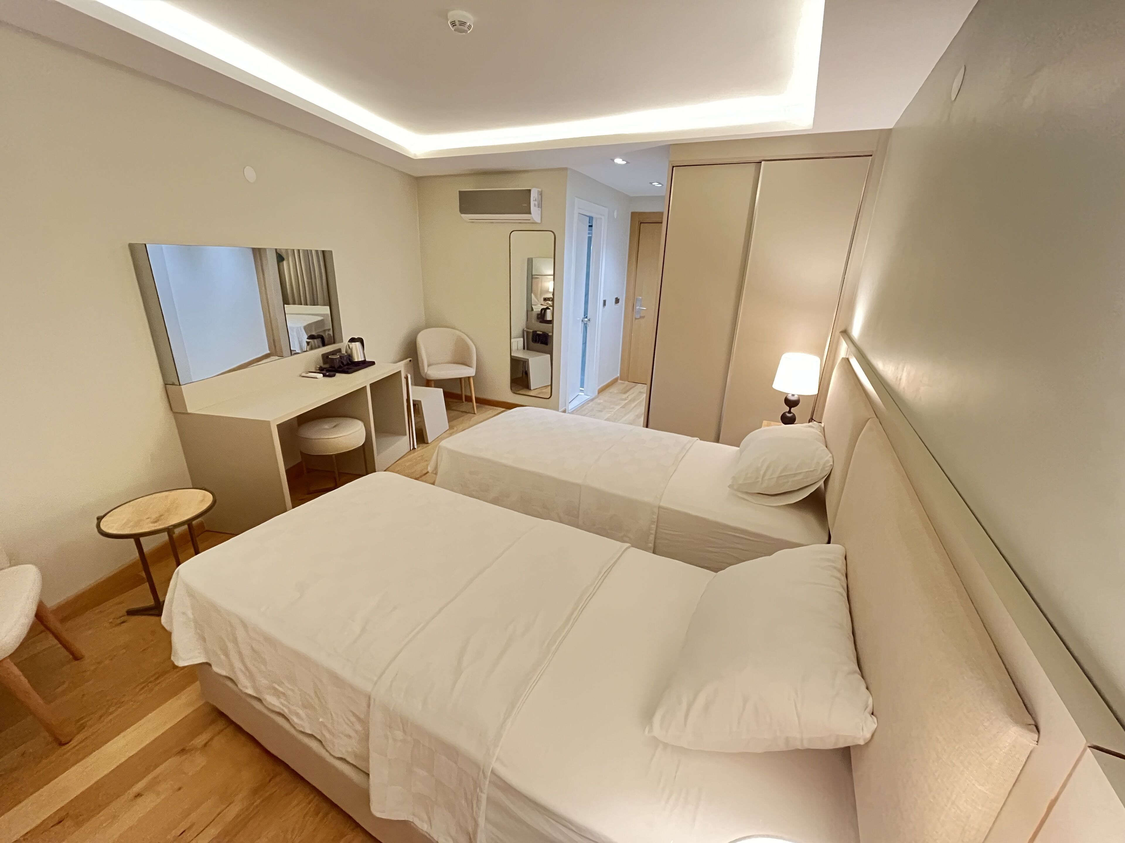 A hotel room with two beds, a desk, a chair, a mirror, and a lamp.