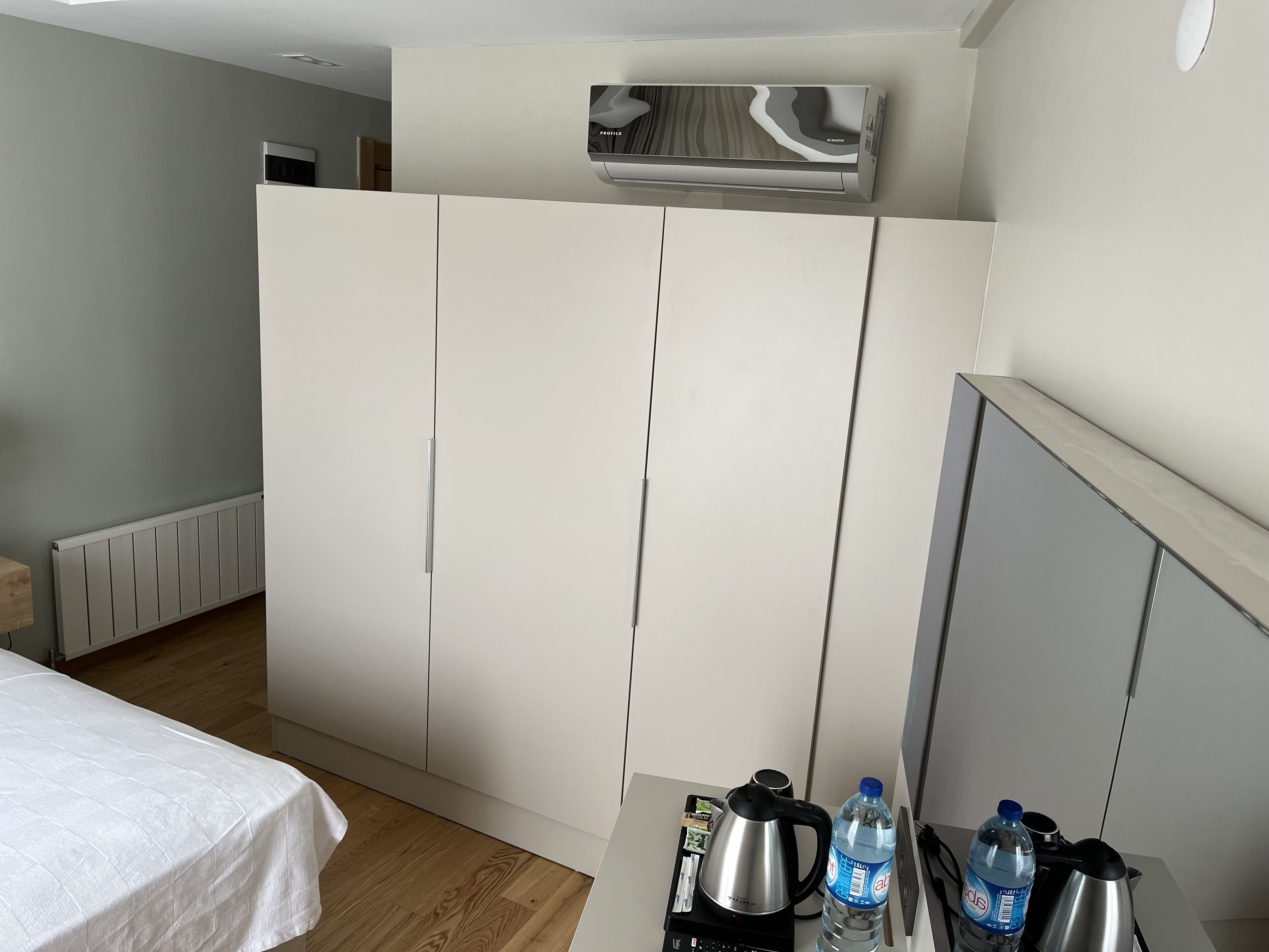 A hotel room with a bed, a kitchenette with a kettle, a water bottle, and a coffee maker.