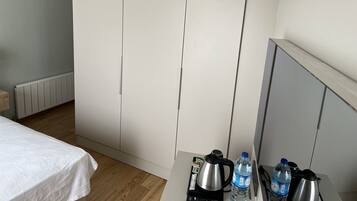 A hotel room with a bed, a kitchenette with a kettle, a water bottle, and a coffee maker.