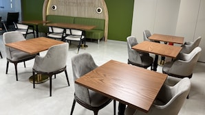 A modern restaurant interior with green walls, wooden tables, and grey upholstered chairs. - Sezer's Oliva Hotel (Ezine)