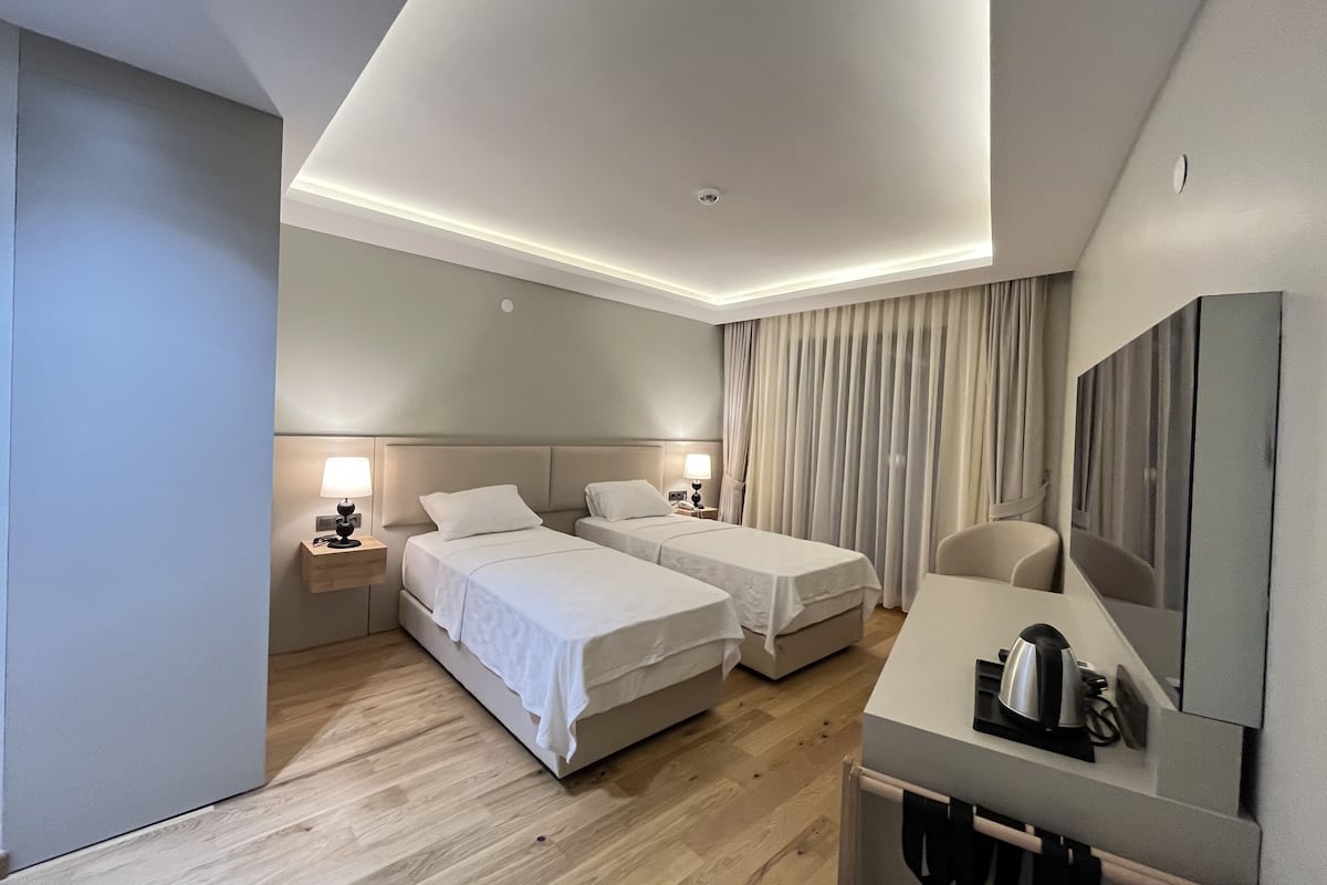 Une chambre d’hôtel avec deux lits, un bureau avec une bouilloire et un grand miroir.