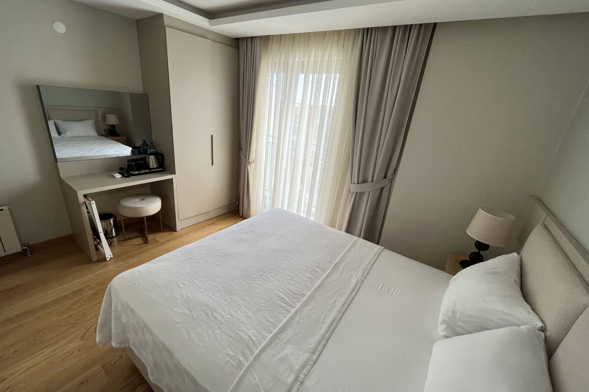 Une chambre d’hôtel avec un lit, un bureau, une chaise, un miroir et une fenêtre avec des rideaux.