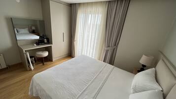 A hotel room with a bed, a desk, a chair, a mirror, and a window with curtains.