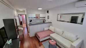 Un ambiente compatto con angolo cottura, divano, televisione e un piccolo tavolo.