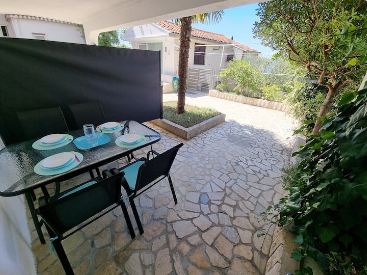An outdoor patio with a table set for dining, surrounded by stone flooring and greenery.