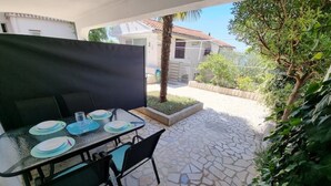 Patio esterno con tavolo apparecchiato per mangiare, circondato da pavimento in pietra e vegetazione.