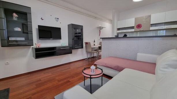 Un soggiorno moderno con un divano bianco, una parete colorata di rosa, una TV a schermo piatto e mobili a incasso.