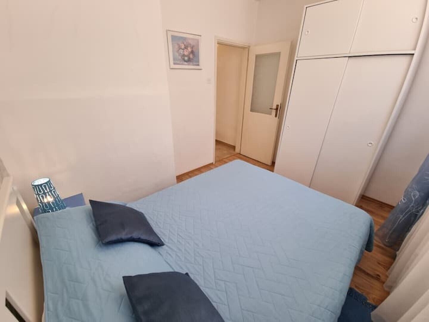 A bedroom with a bed, pillows, a wardrobe, and a door leading to another room.