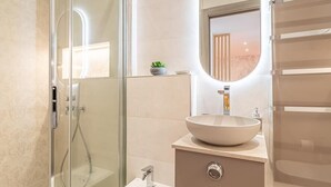 A modern bathroom with a glass shower enclosure, a round mirror, and a beige vanity with a vessel sink. - Le 182 Promenade du Soleil, Tout Juste Rénové, Azur Riviera (Menton)