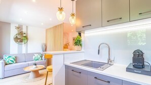 A modern kitchen with a built-in sink, a dining area with a round table, and a living room with a sofa and decorative plants. - Le 182 Promenade du Soleil, Tout Juste Rénové, Azur Riviera (Menton)