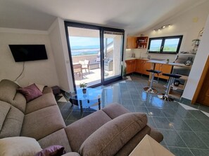 A modern living room with a large sectional sofa, a glass coffee table, and a view of a balcony with outdoor furniture.