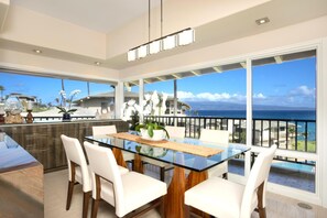 Une cuisine moderne avec une table à manger en verre, des chaises blanches et une vue sur l’océan.