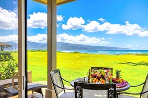 A patio with a table set for dining, overlooking a grassy area and a view of the ocean with mountains in the distance. - Kapalua Bay Villas by KBM (Kapalua)