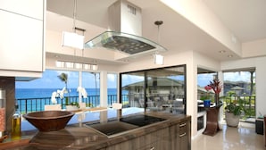 A modern kitchen with a large island, a glass top stove, and a view of the ocean.
