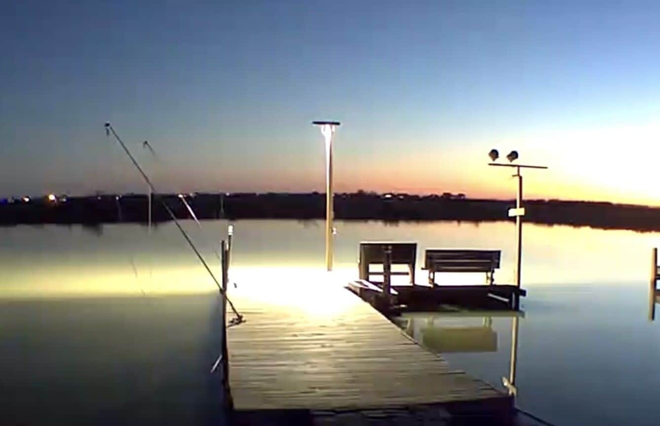 A wooden dock extending into calm water with a bench and a lamp post.