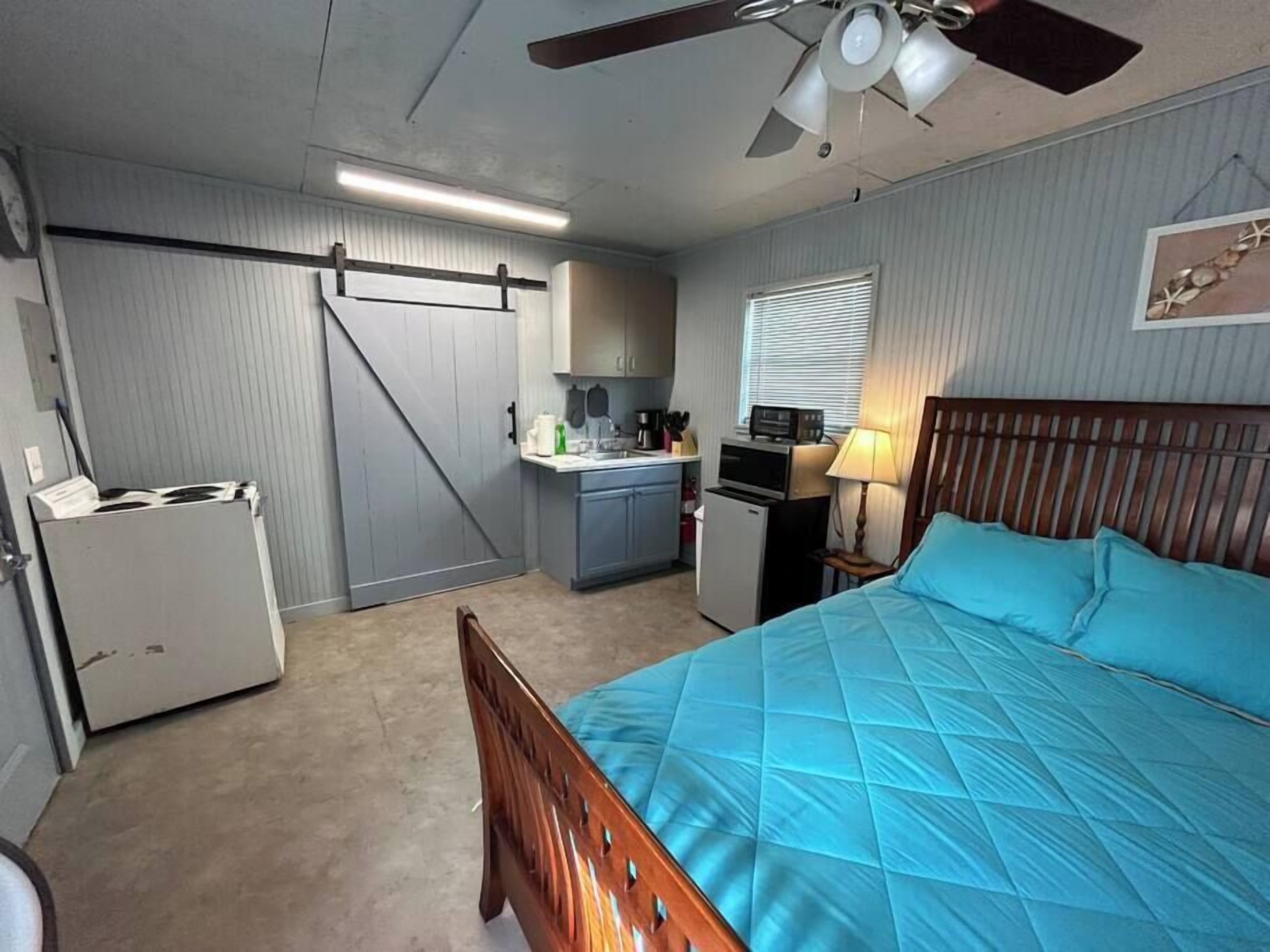 A compact room with a bed, kitchenette, and a ceiling fan.