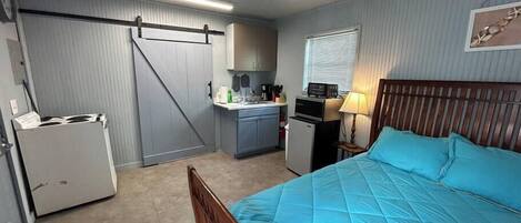 A compact room with a bed, kitchenette, and a ceiling fan.