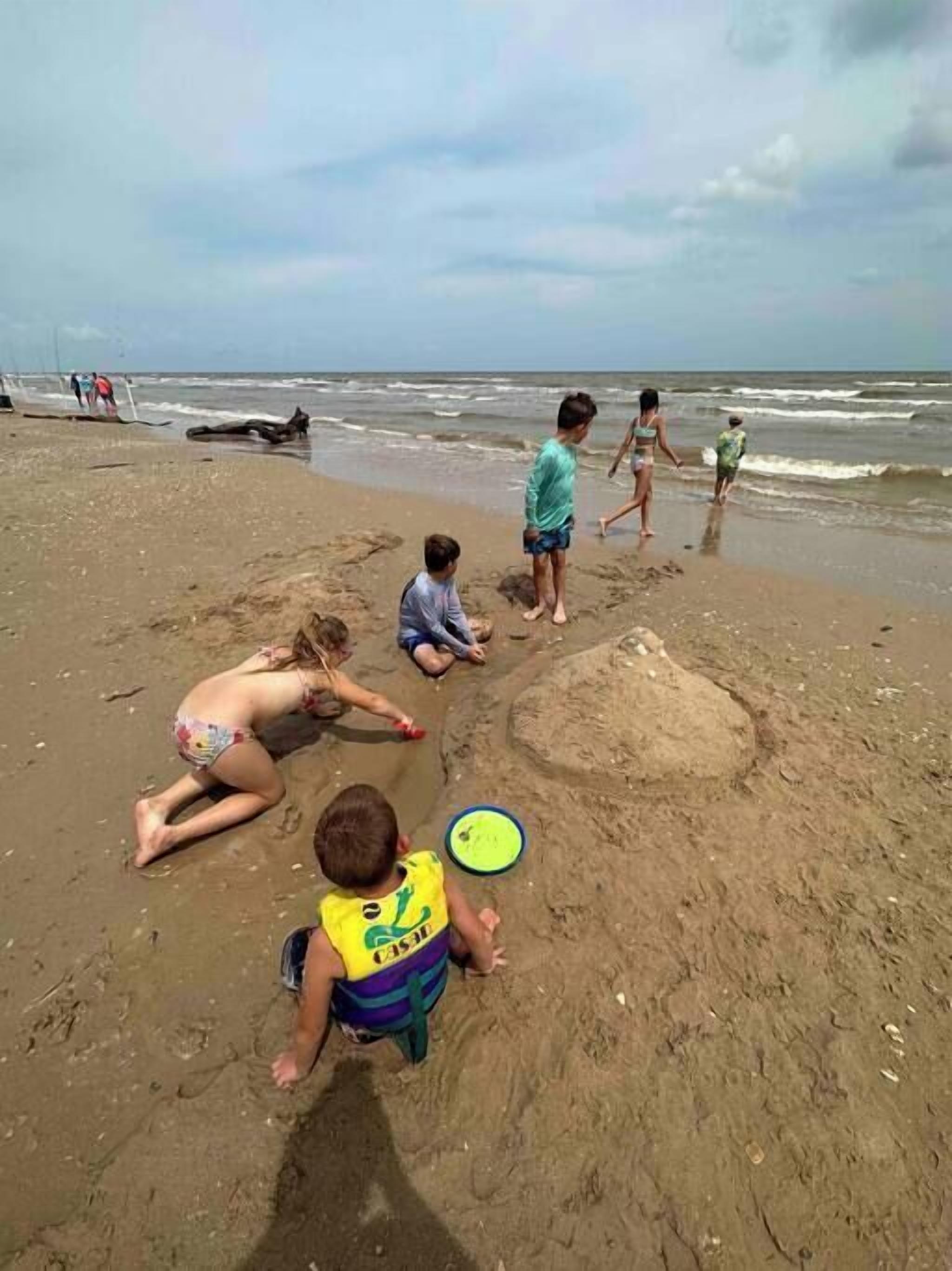 Une plage de sable où des gens jouent et où un enfant porte un gilet de sauvetage.