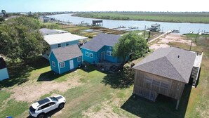 Una zona residencial con dos casas azules, un coche blanco y un muelle junto a un cuerpo de agua.