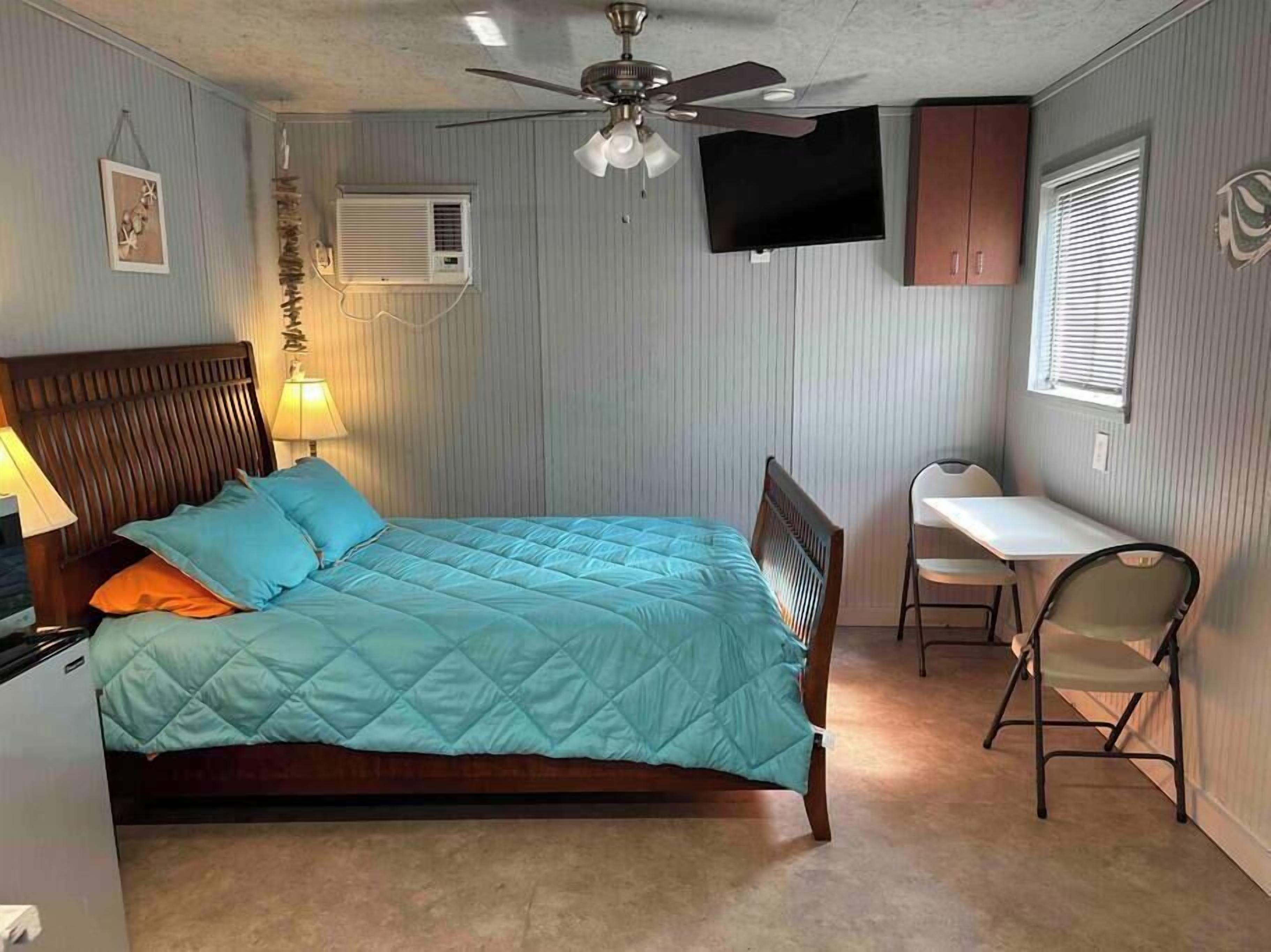 Een slaapkamer met een bed, een bureau, een stoel, een plafondventilator, airconditioning en een televisie.